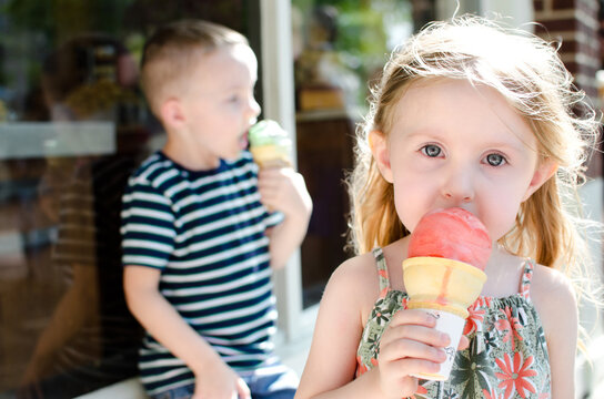 A Little Girl And Boy Enjoying Ice Cream Outside Of A Shop
