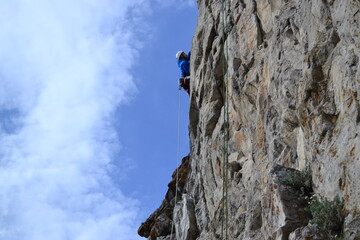 A rock climber in a white helmet climbs a rock in sunny weather