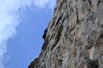 A rock climber in a white helmet climbs a rock in sunny weather