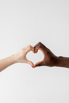 Multiethnic love. Racial tolerance. Peace harmony. Support cooperation. National partnership. Conceptual art. White female and black male hands holding together heart figure isolated light.