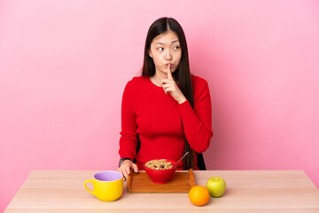 Young Chinese girl  having breakfast in a table showing a sign of silence gesture putting finger in mouth