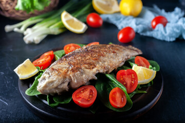 Grilled fish with tomatoes, spinach on a wooden board. Delicious and light dinner