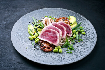 Modern style traditional Japanese gourmet seared tuna fish steak tataki with soba noodles and stir-fried vegetables served as close-up on a Nordic design plate with copy space