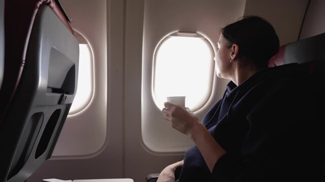 woman drinks water from a paper cup on board an airplane