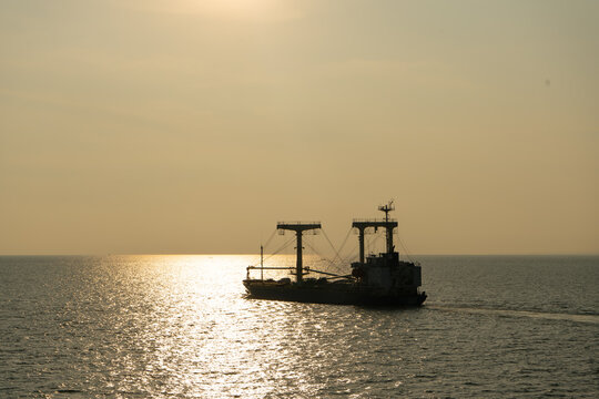 A cargo ship is sailing towards the sunset in the middle of the ocean.