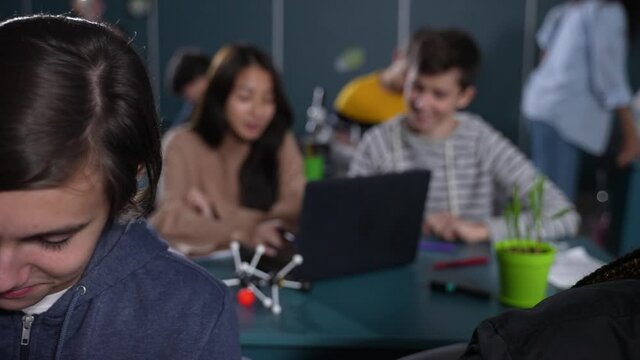 Cute asian schoolgirl and caucasian schoolboy working together on joint educational project at laptop during science lesson. Friendly multiracial high school students communicating during classes