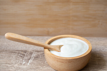 White yogurt in a wooden cup with a wooden spoon