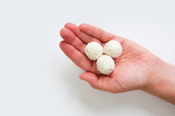 Three round candies of white chocolate truffles covered in shredded coconut on man's palm isolated on white background with clipping path. Handmade candies, sweet balls. Selective focus.