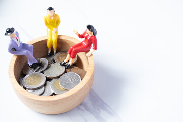 Miniature people. Sitting on a wooden bowl with coins on a white background. Money saving concept....