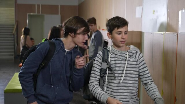 Closeup of impudent caucasian students taking tablet of african american schoolgirl standing by school locker. Shameless teen hooligans stealing digital tablet of dark-skinned classmate