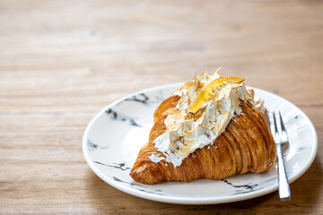 A croissant with lemon on top from white petrified ceramic placed on a wooden table, the concept of combining more flavorful croissants
