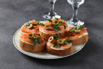 Canapes of salted salmon, green olives and parsley on croutons of white bread on dark gray background. Festive snack.
