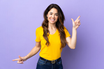 Woman over isolated purple background pointing finger to the laterals and happy