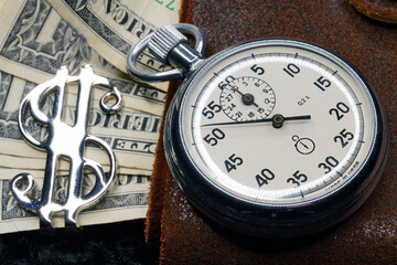 Dollar close-up. Money macro shot. The stopwatch lies on paper banknotes and a leather wallet. Clock, watch, timepiece, timer, clock face, mechanical device, speedometer                            