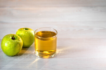 One glass of apple juice with green apples in the sunset background. Nice white wood table. Summer day. Good mood.