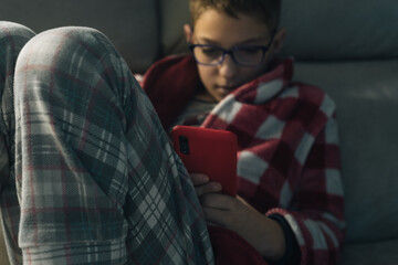 CHILD IN DRESSING GOWN ON SOFA USING MOBILE PHONE