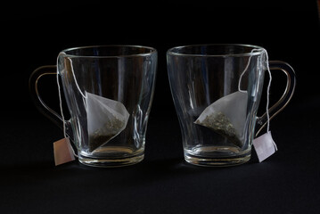 Two glass transparent heat-resistant mugs with tea bags - pyramids. Green tea. Black background