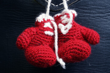 Fototapeta na wymiar Red summoned boxing gloves with white shoelaces hang on a black background. Needlework. Crocheted souvenir. Gift 