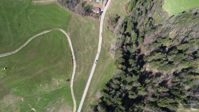 Top down aerial following a tractor driving on a small street in the Swiss alps.