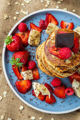 Healthy banana oatmeal pancakes stack with strawberries, bananas, raspberries and chocolate. Easy making gluten free morning breakfast or brunch. Delicious heap of pancakes with vibrant, fun, colors.