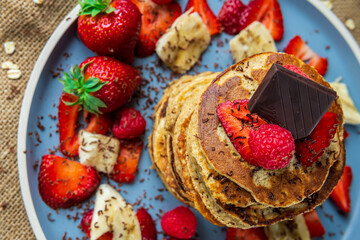 Healthy banana oatmeal pancakes stack with strawberries, bananas, raspberries and chocolate. Easy making gluten free morning breakfast or brunch. Delicious heap of pancakes with vibrant, fun, colors.