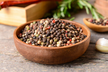 Bowl with peppercorns on wooden background