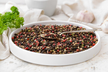 Plate and spoon with peppercorns on light background