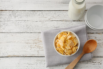 Bowl with tasty cornflakes and bottle of milk on light wooden background