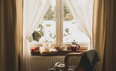 Winter relax at cozy home. Hot tea, teapot and book by the window.