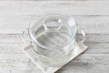 Stylish cooking pot with water on light wooden background