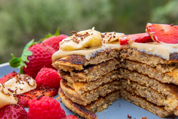 Healthy banana oatmeal pancakes stack sliced with strawberries, bananas, raspberries, chocolate and halva spread. Easy gluten free morning breakfast or brunch. Delicious fluffy pancakes heap, Vibrant.