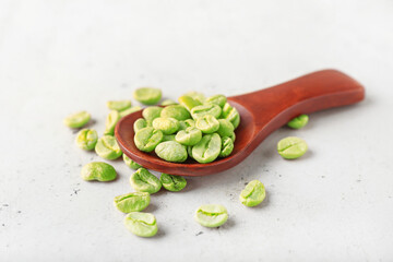 Spoon with green coffee beans on light background