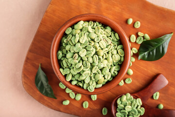 Bowl and spoons with green coffee beans on color background