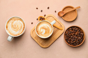 Cups of hot cappuccino and plate with coffee beans on color background