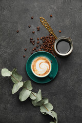 Cup of hot cappuccino and coffee pot on dark background