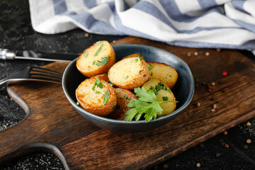 Bowl of tasty baked potatoes with parsley on dark background