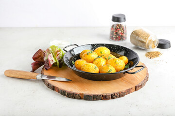 Frying pan of tasty potatoes with parsley on light background