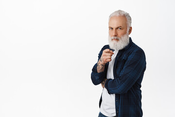 Serious old man with tattoos pointing finger at camera and frowning, inviting you, scolding grandchildren, being a boss, choosing someone, standing over white background