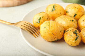 Plate of tasty baked potatoes with parsley on light background
