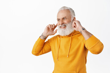 Handsome senior man listen music on wireless earphones and smiling, looking aside at logo. Hipster old man enjoying perfect sound of earbuds, white background