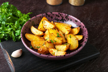 Plate of tasty fried potatoes with parsley on dark background