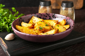 Plate of tasty fried potatoes with parsley on dark background