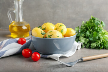 Bowl of tasty boiled potatoes with parsley on grey background