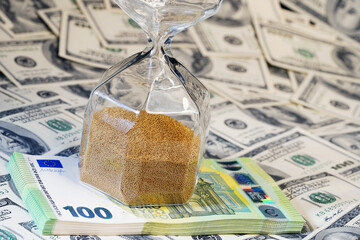 Time is money. Hourglass stand on a layer of notes. Dollars. Watch. Clock. Countdown. American currency. Dollars                                