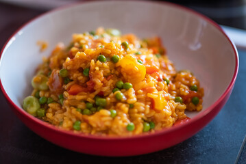 Close up of a healthy, nutritious and homemade vegetable paella in a red dinner bowl with selective focus, shallow depth of field and bokeh
