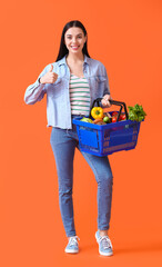 Obraz na płótnie Canvas Young woman with shopping basket showing thumb-up on color background