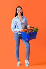 Young woman with shopping basket on color background