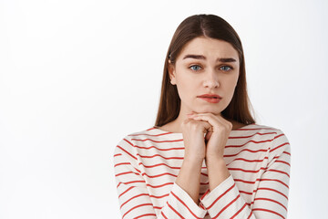 Close up of hopeful sad girl, making coy needy face, frowning and begging for help, asking for favour, need something, standing over white background