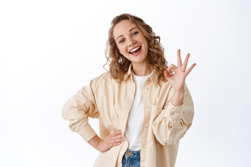 Attractive blond girl smiling, say yes, showing okay sign, praising good job, making compliment,...