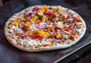 Close and selective focus of a readymade frozen stone baked thin sweet chilli chicken pizza on a baking mat ready to be cooked in the oven for Saturday night dinner